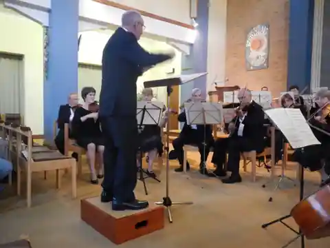 The conductor on a small podium leading the string section in a church setting